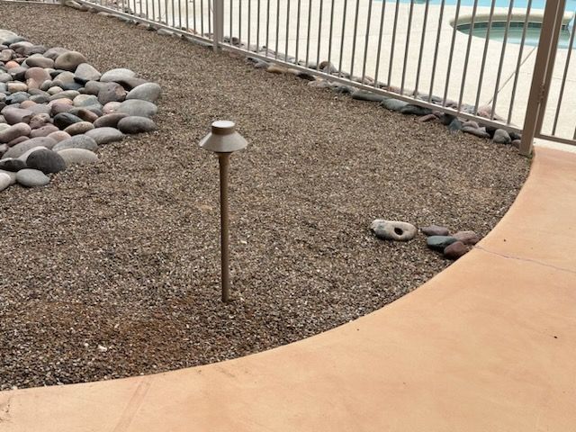 Ground-level landscaping with rocks, gravel, and a pathway next to a fence and pool.