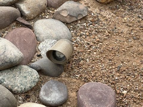 Rocks and gravel surround a small, tan lighting fixture with a lens.