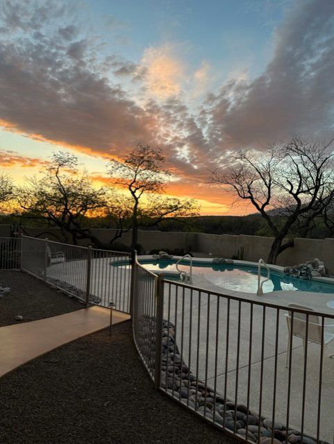 Sunset over a pool surrounded by a fence and bare trees. Orange and blue sky.