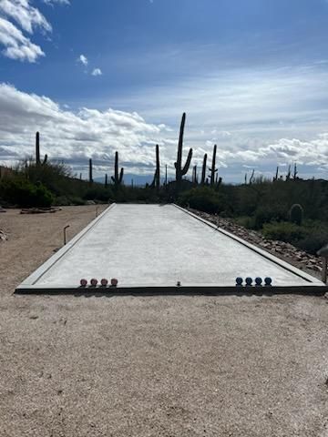 Bocce ball court in a desert landscape. Red and blue bocce balls are scattered on the court, saguaro cacti in the background.