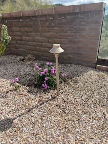 A beige path light next to pink flowers, gravel bed, brick wall in background.