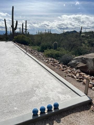 Bocce ball court with blue balls lined up, desert landscape with cacti in the background, cloudy sky.