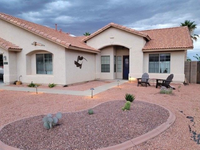 Tan stucco house with red-tile roof, arid landscaping, and walkway leading to the front door.