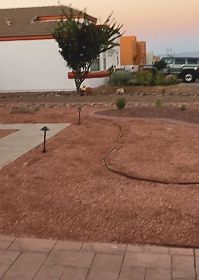 A residential landscape with red gravel, a tree, and a curved path. A house and SUV are in the background.