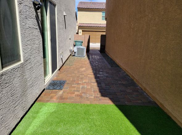 Narrow brick pathway between two buildings with artificial turf.