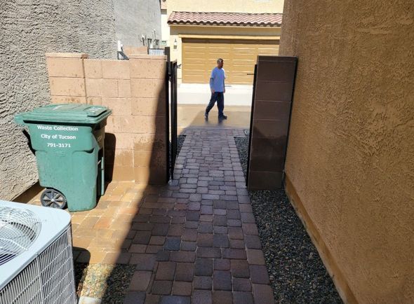 Narrow brick path with a gate, trash can, and person walking.