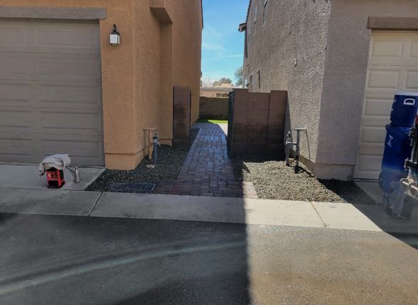 Narrow alley between two buildings, paved walkway with gravel edges.