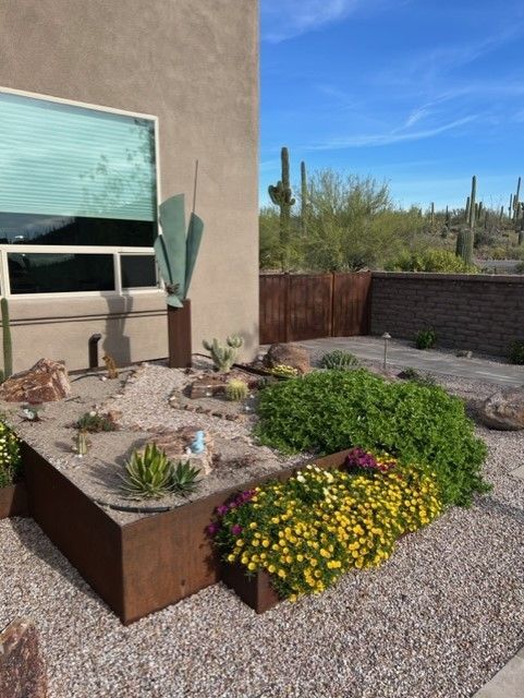 Desert landscape with a metal planter box filled with plants and rocks, next to a building.