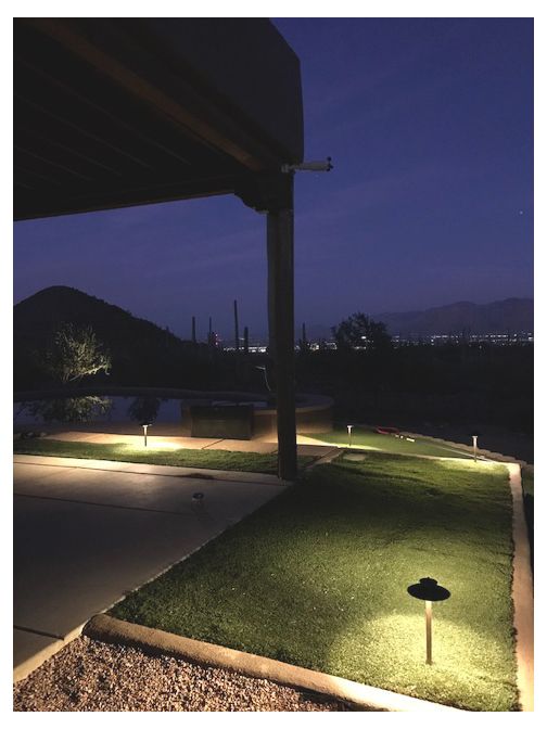 Night scene: pathway and lawn lit by landscape lights; dark sky, mountain backdrop.