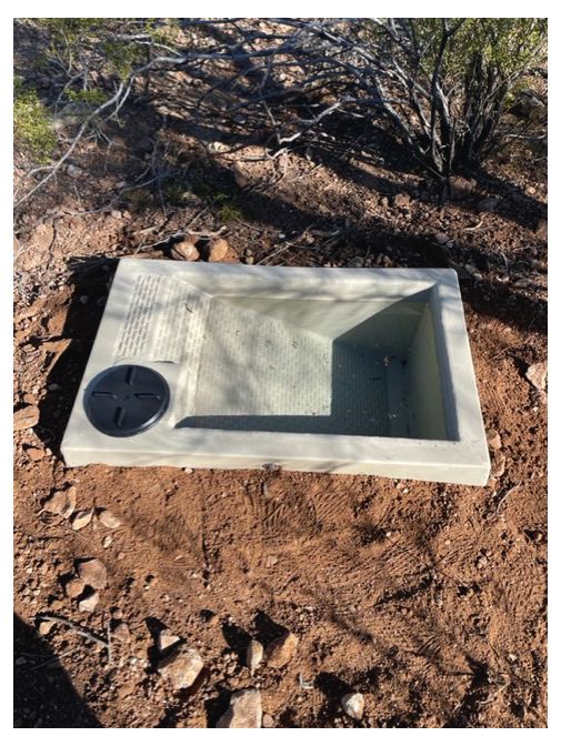 Rectangular concrete water trough with a black cover in a dry, desert environment.