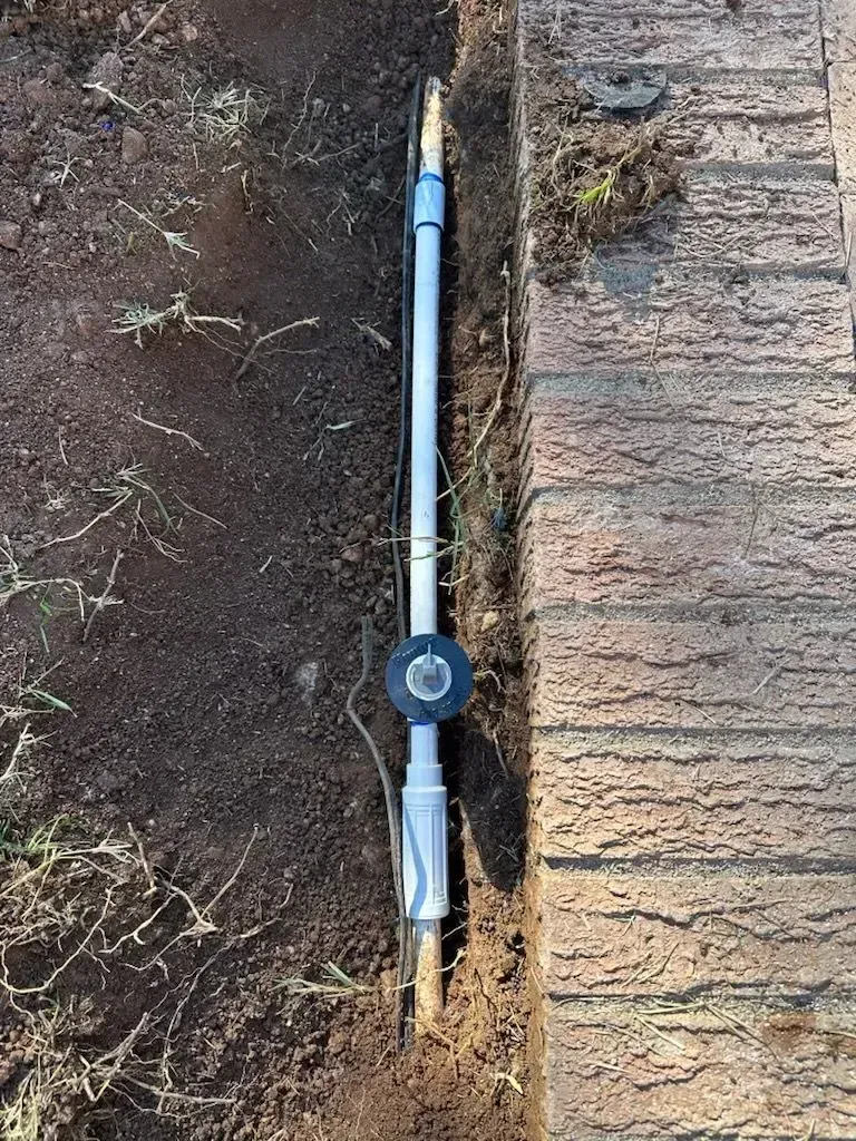 A buried irrigation system pipe runs along a brick edge in dark soil.