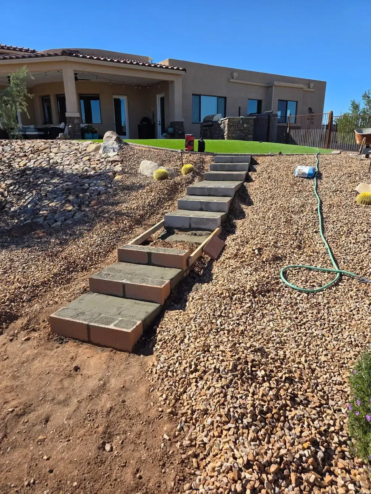Staircase under construction in a sloped backyard, made of bricks and concrete. Brown gravel surrounds.