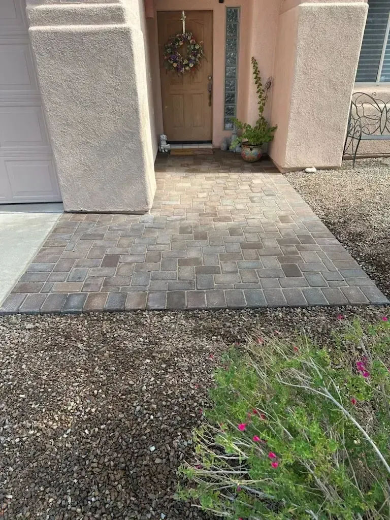 Brick walkway leading to a front door with a wreath. Beige stucco columns flank the doorway.