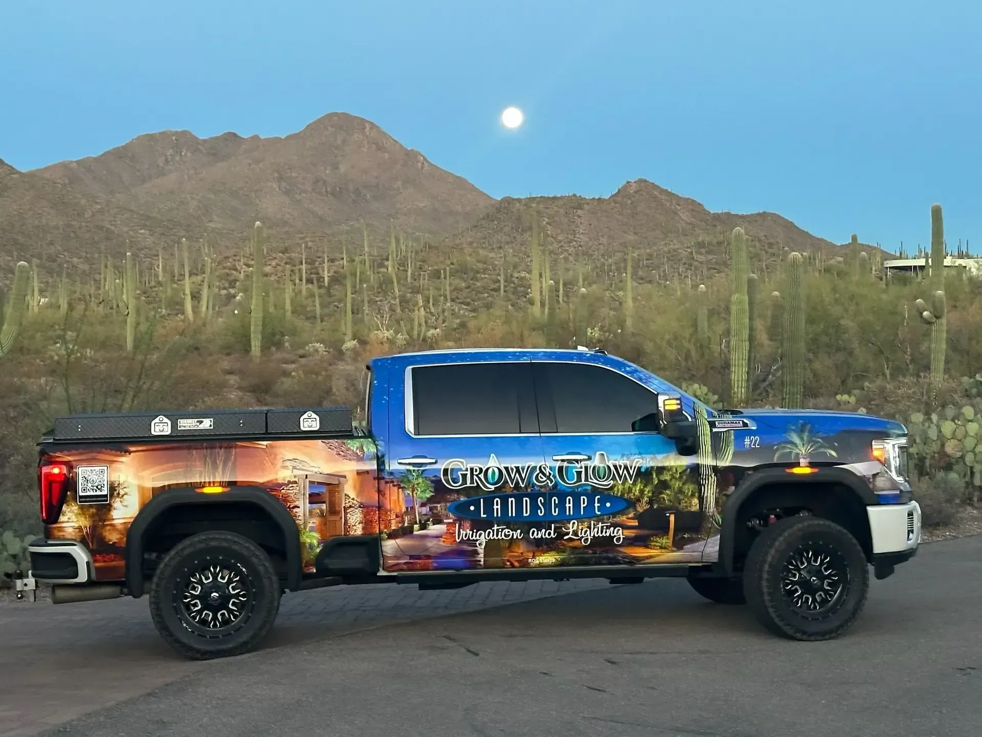 Truck with landscape company wrap parked in front of desert mountains under a full moon.