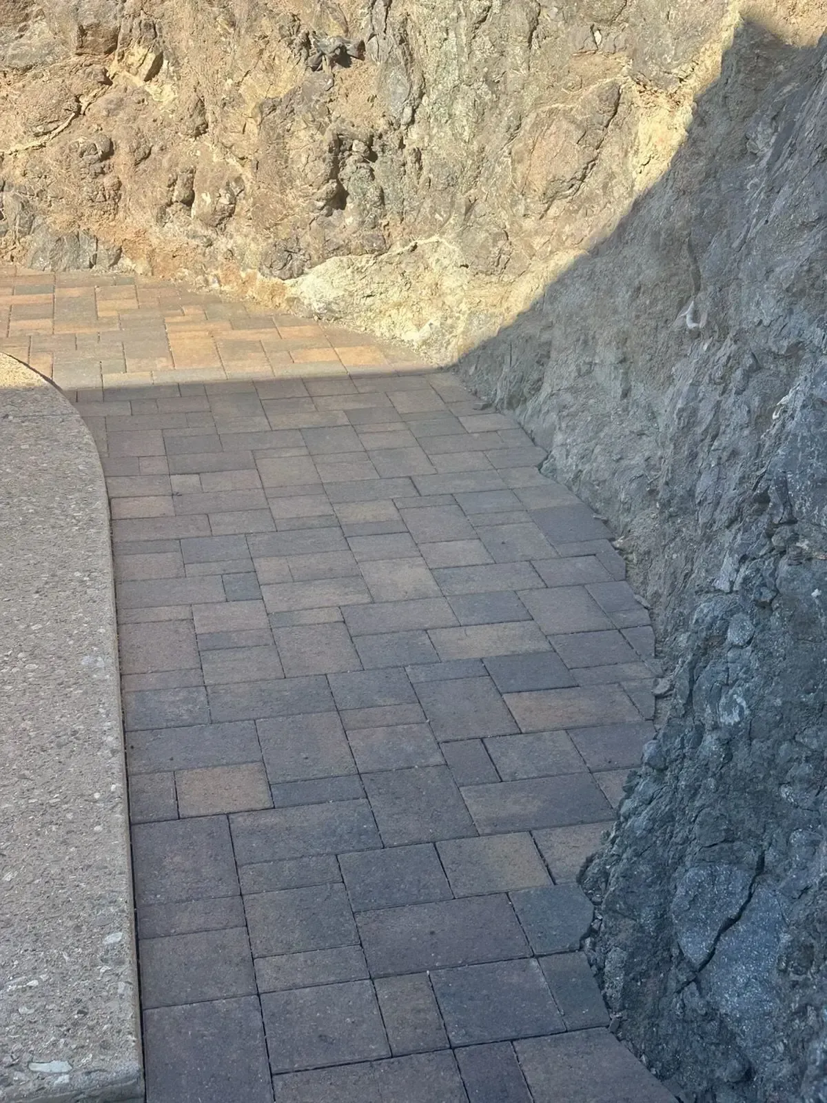 Paver walkway between rock walls, leading towards an unseen area.