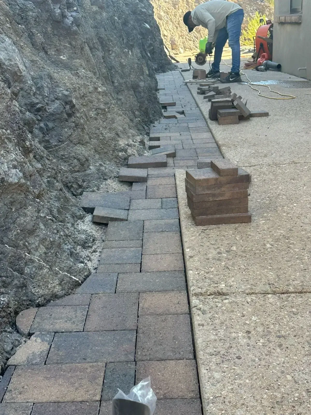 A person laying brick pavers next to a rocky hillside.