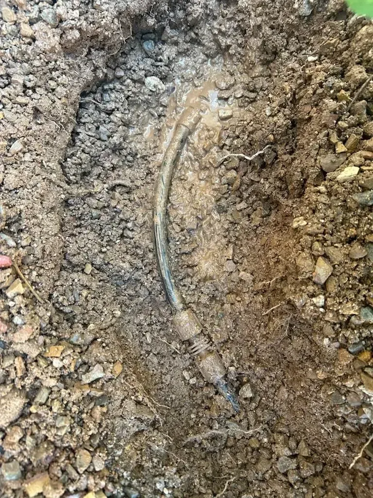 A curved, silver cable partially buried in brown soil and gravel.