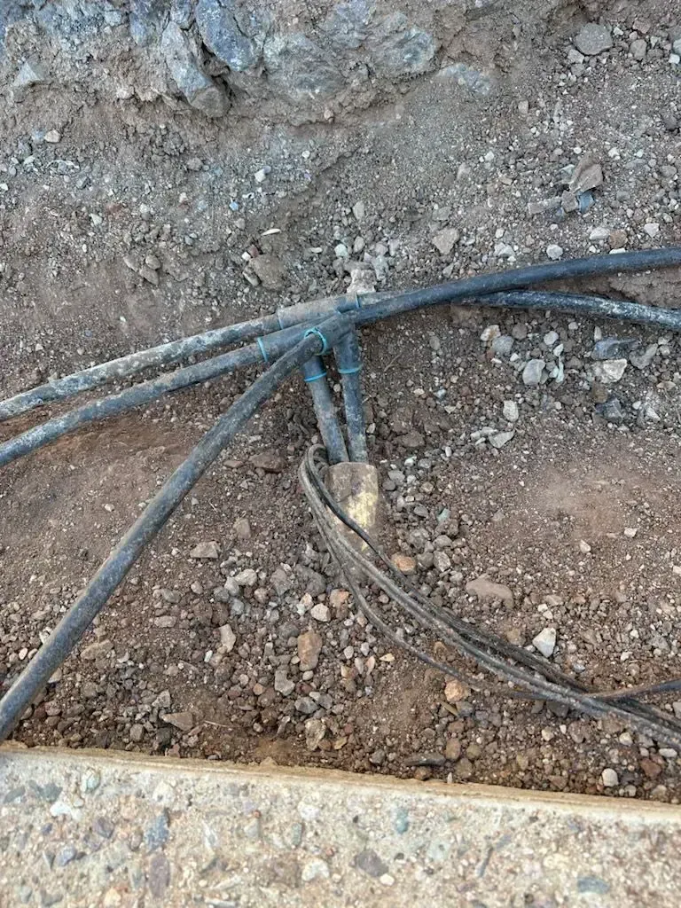 Black cables joined, partially buried in dirt and gravel, likely for utility.