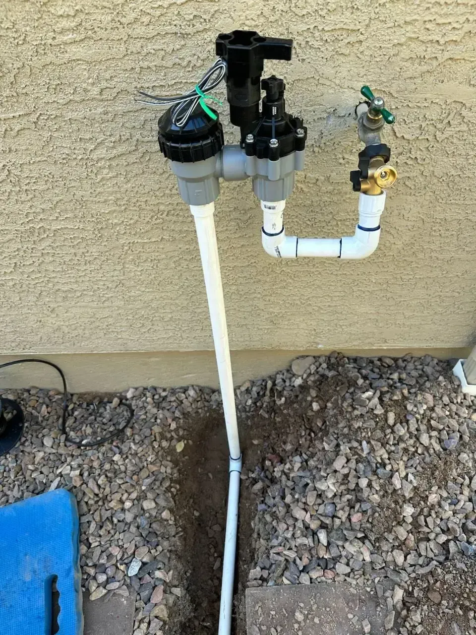 Irrigation system components attached to a stucco wall, including valves, pipes, and electrical wiring.