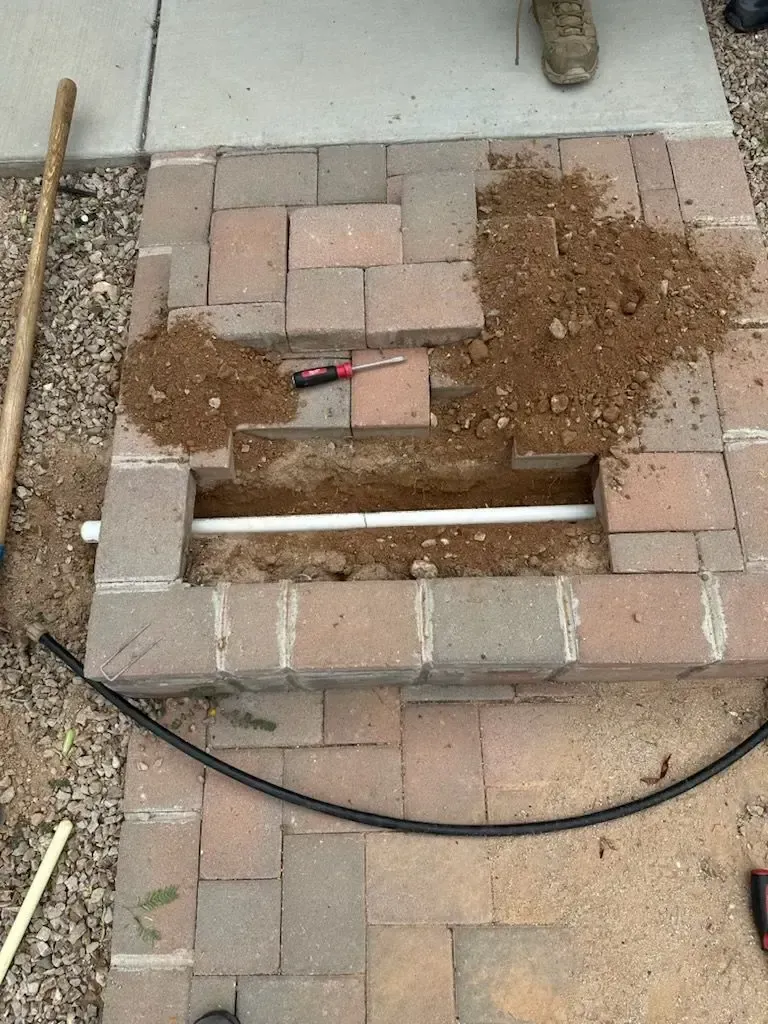 A trench dug in brick pavers with a white pipe running through, dirt piled next to it.