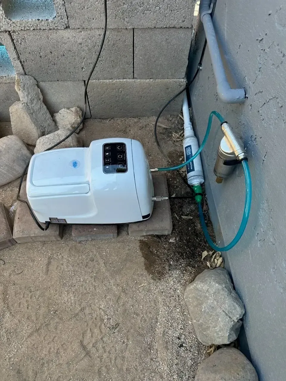 White water pump system near a concrete block wall, with filters and tubing.