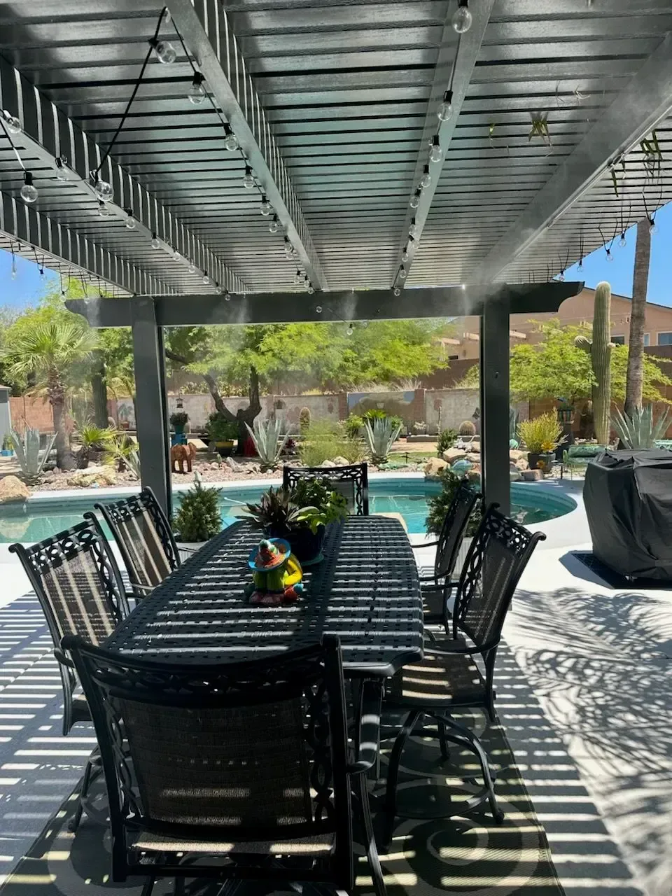 Patio with dining table, chairs, and pool, under a shaded pergola with string lights.
