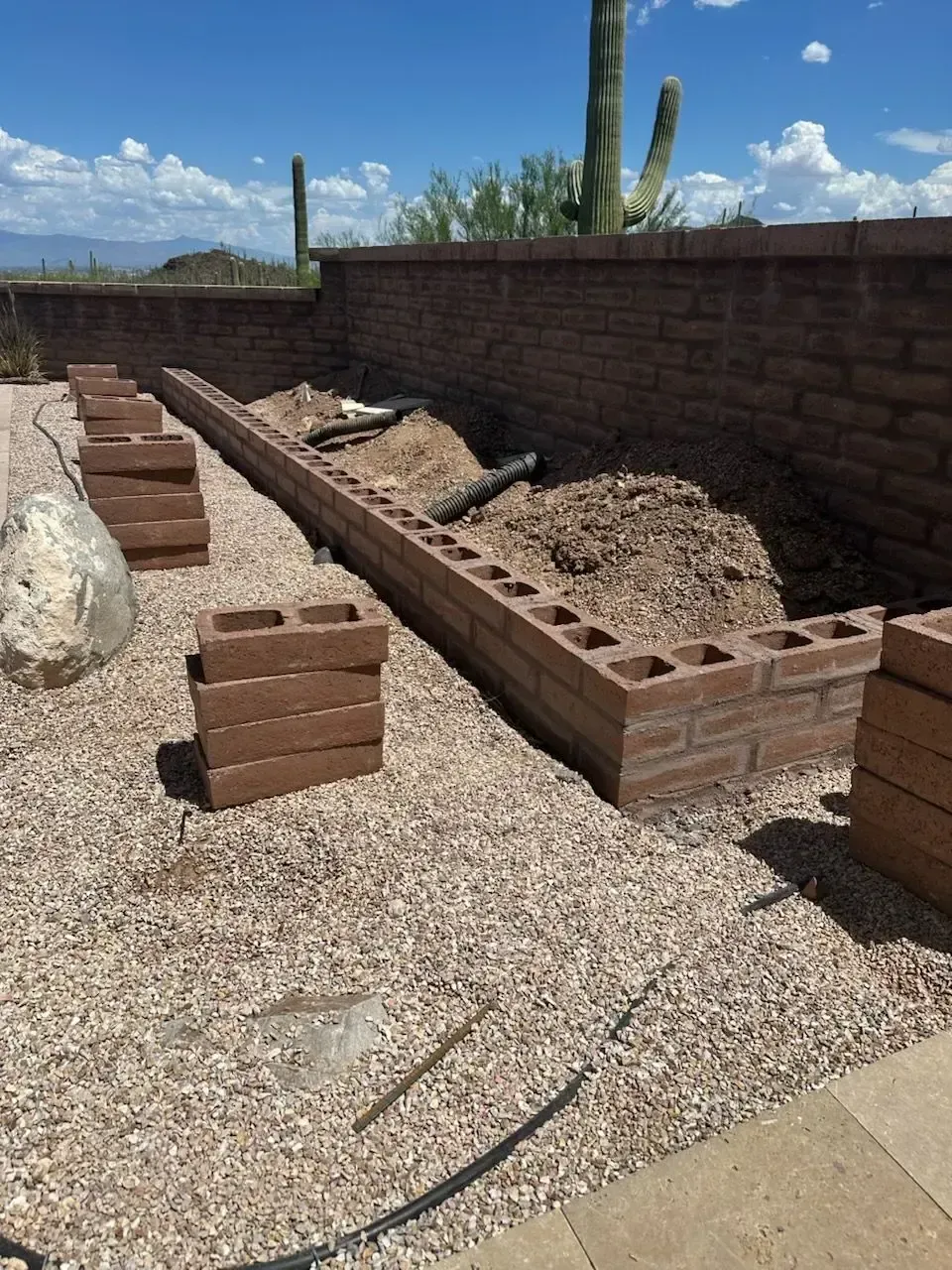 A partially built brick retaining wall in a desert landscape with gravel ground cover.