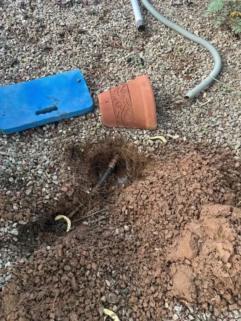 A broken irrigation system with a terracotta pot, blue kneeling pad, and hose on the ground.