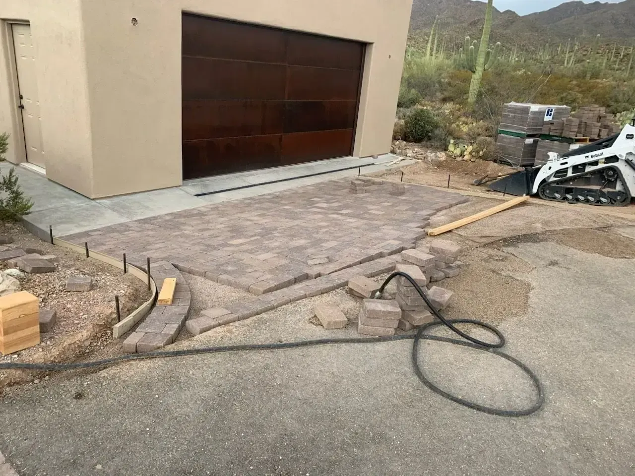 Brick patio construction in progress next to a garage. A Bobcat tractor sits in the background.