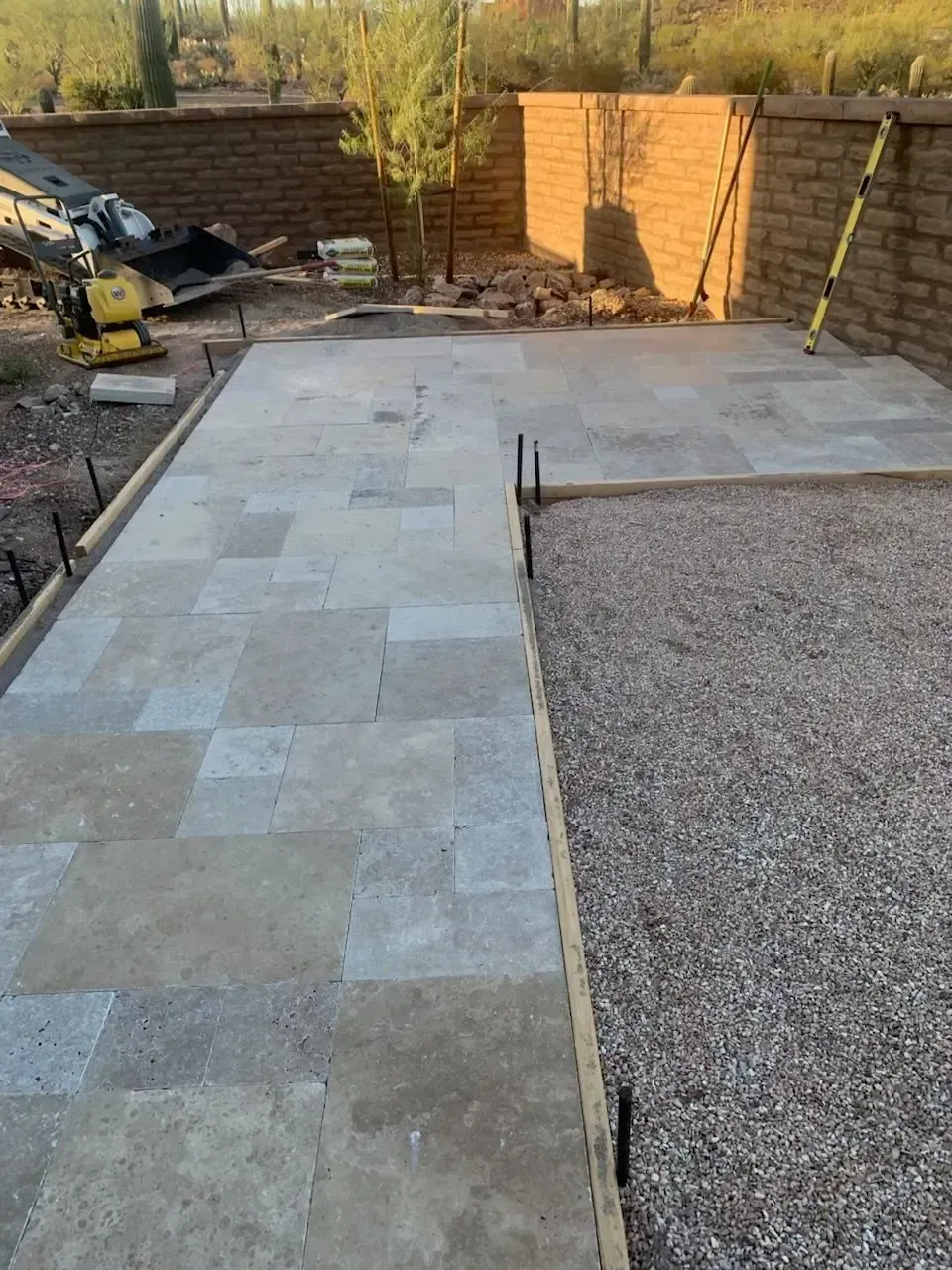 Concrete patio under construction with gravel base, surrounded by brick walls and tools.