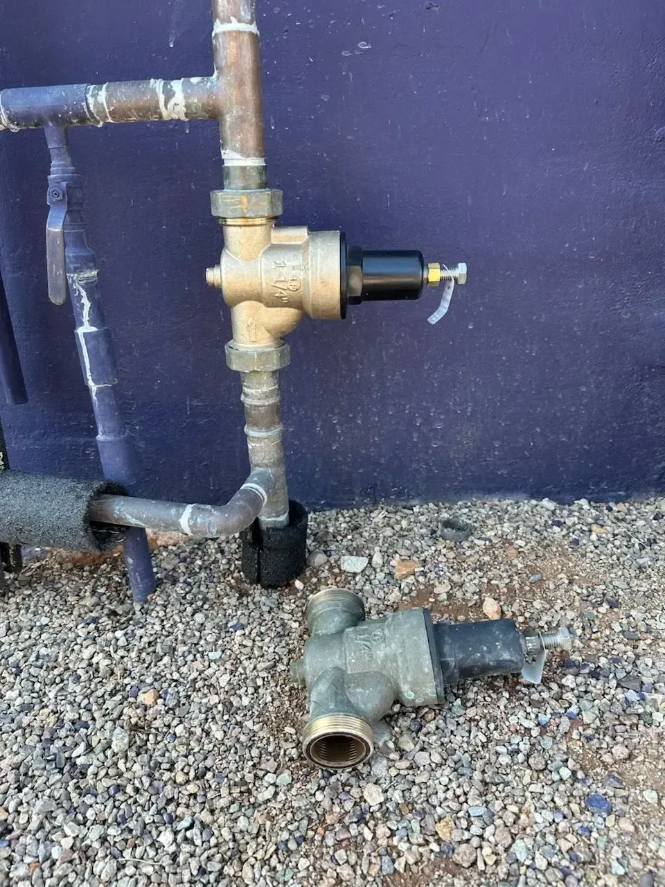 Copper pipes and valves, one vertical with a black component, another valve on the ground.