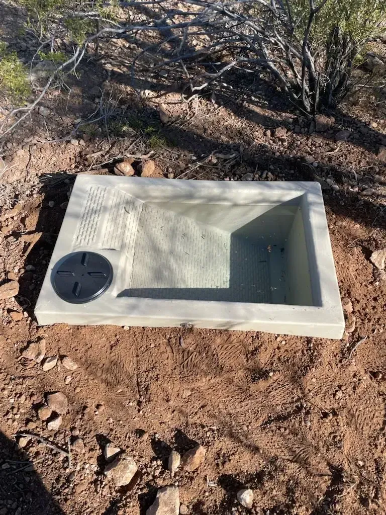 Concrete washbasin with drain cover, set in arid, brown earth.