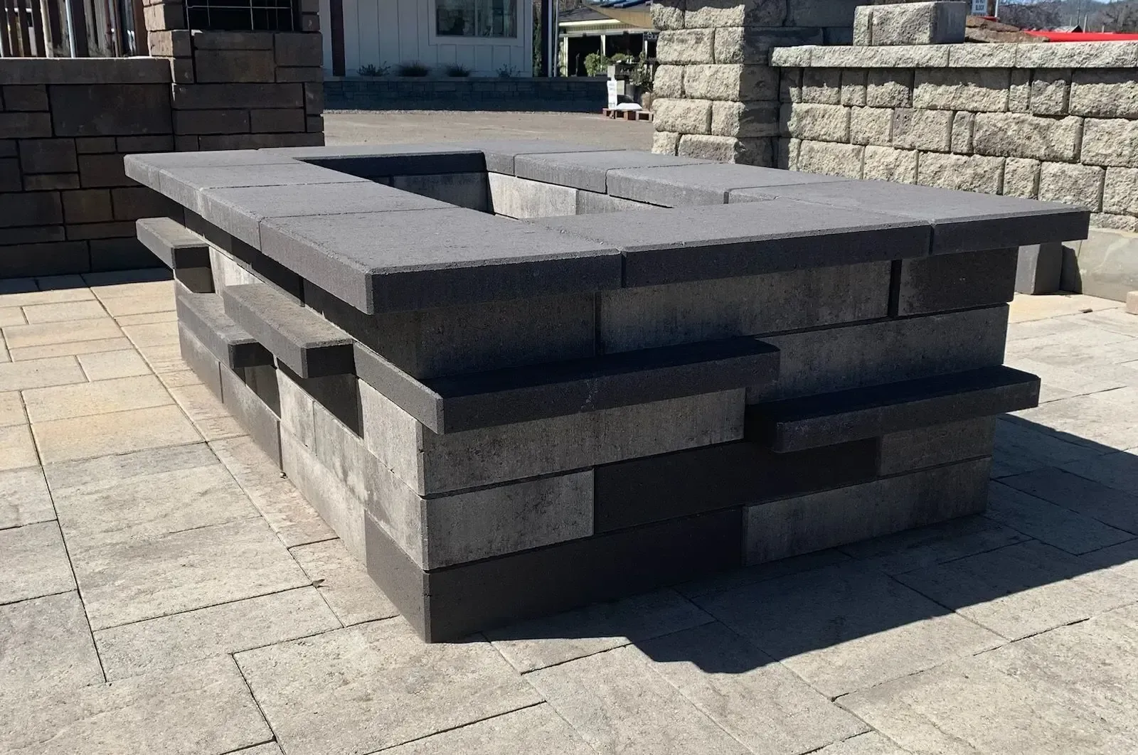 Square gray brick fire pit on a paver patio, with a rectangular opening.
