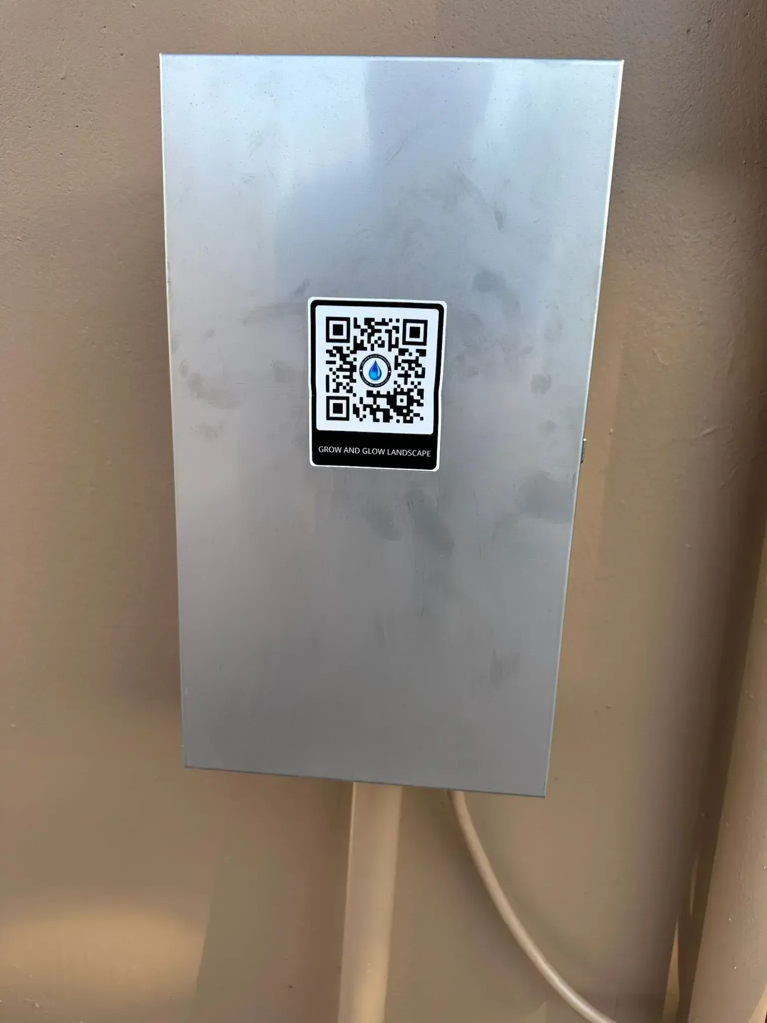Silver box with QR code attached to a wall, conduit and cable visible.