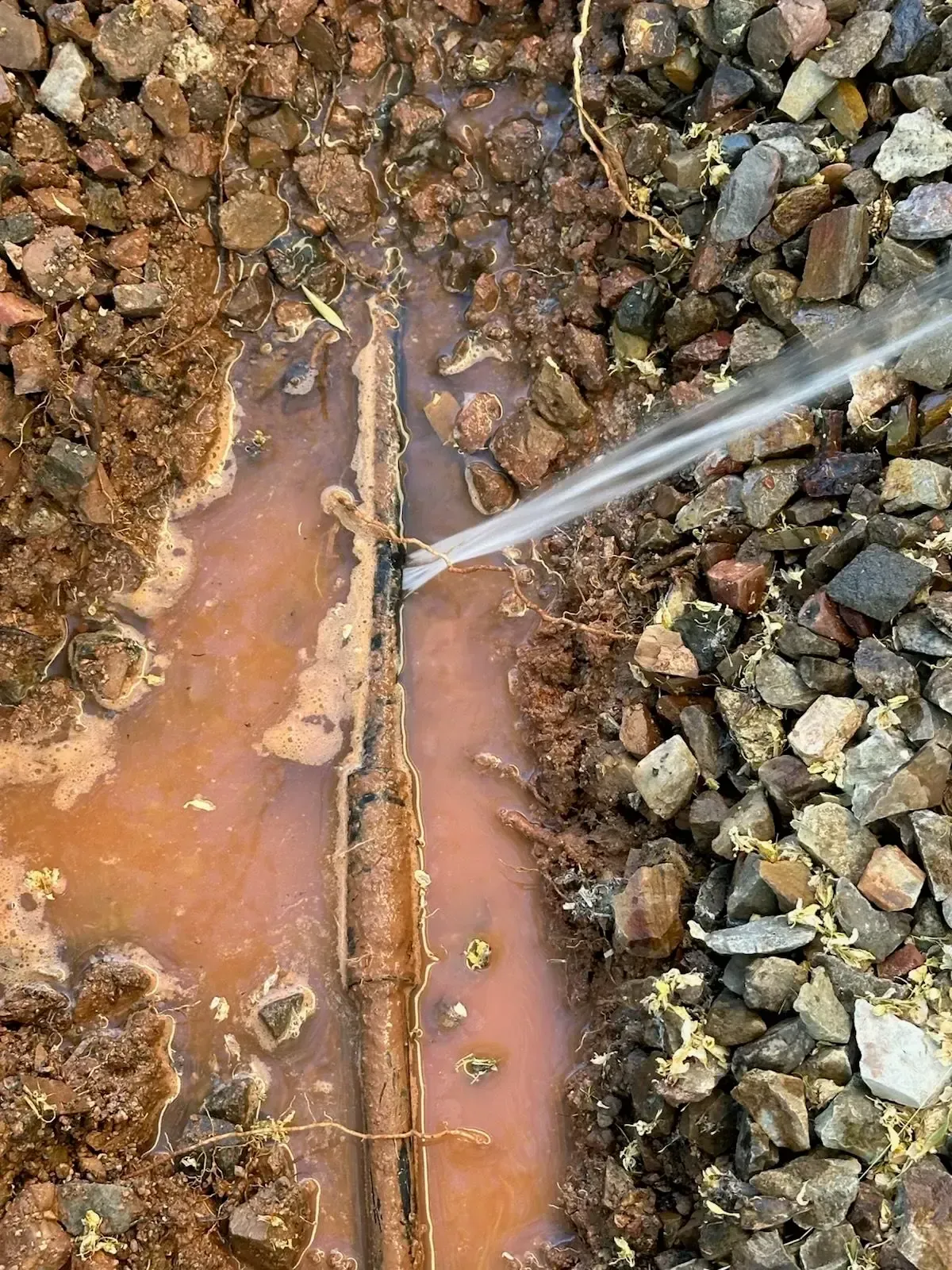 Leaking pipe spews water; surrounded by wet dirt and gravel.