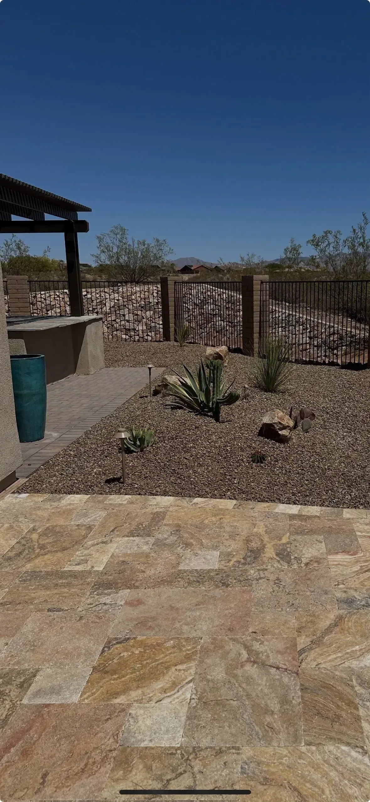 A desert landscape with a stone patio, garden, and wooden gate under a blue sky.