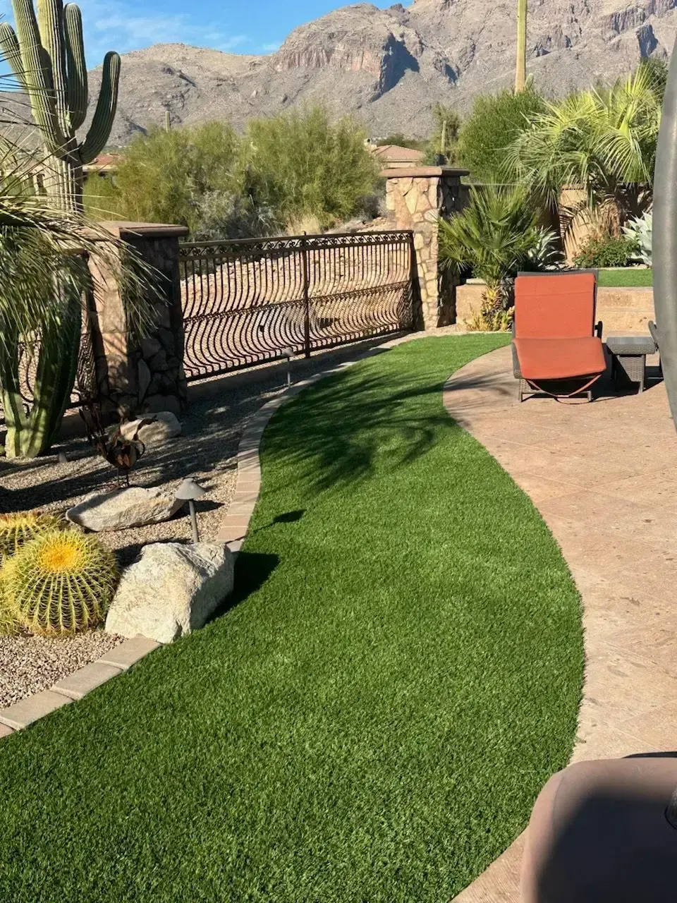 Green artificial turf pathway in a desert landscape, bordered by stone and cacti, leading to a decorative gate.