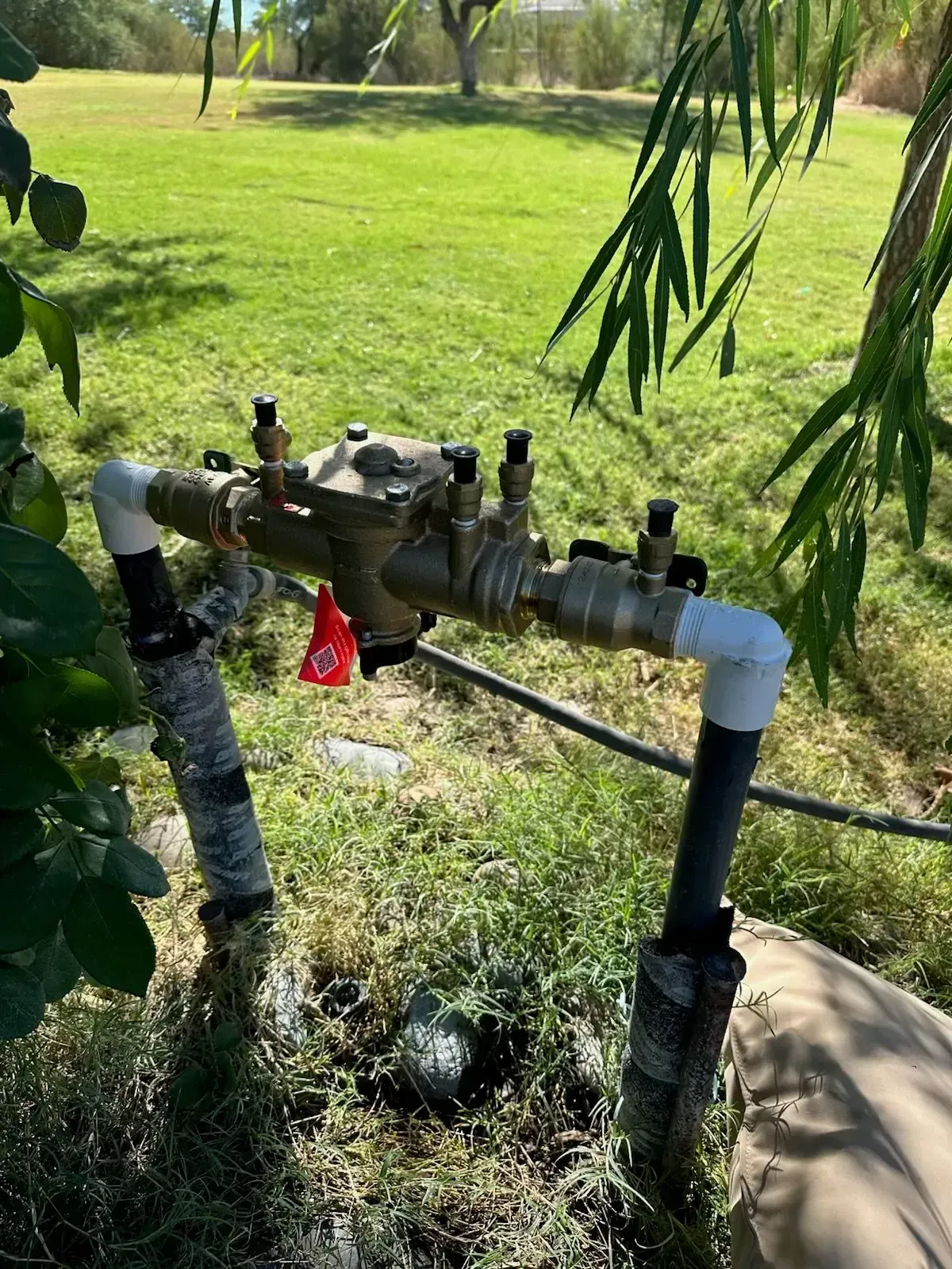 Backflow preventer in a grassy yard, with black pipes and brass components.