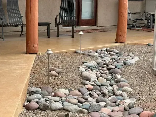 Gravel and stone landscaping with outdoor lights next to a covered porch with furniture.