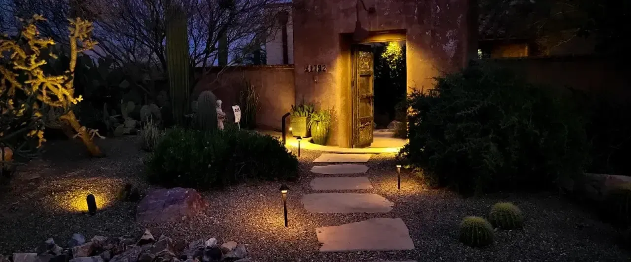 Stone path leads to a lit doorway in a desert-like garden at night.