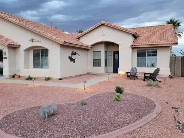 Beige house with red tile roof, Arizona landscaping, cloudy sky.