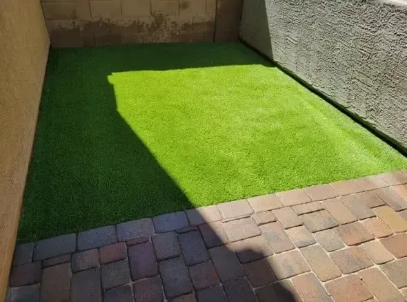 Green artificial turf area between beige walls and brick patio.