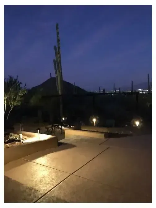 Nighttime outdoor scene with lit pathway, desert vegetation, and mountain silhouette.