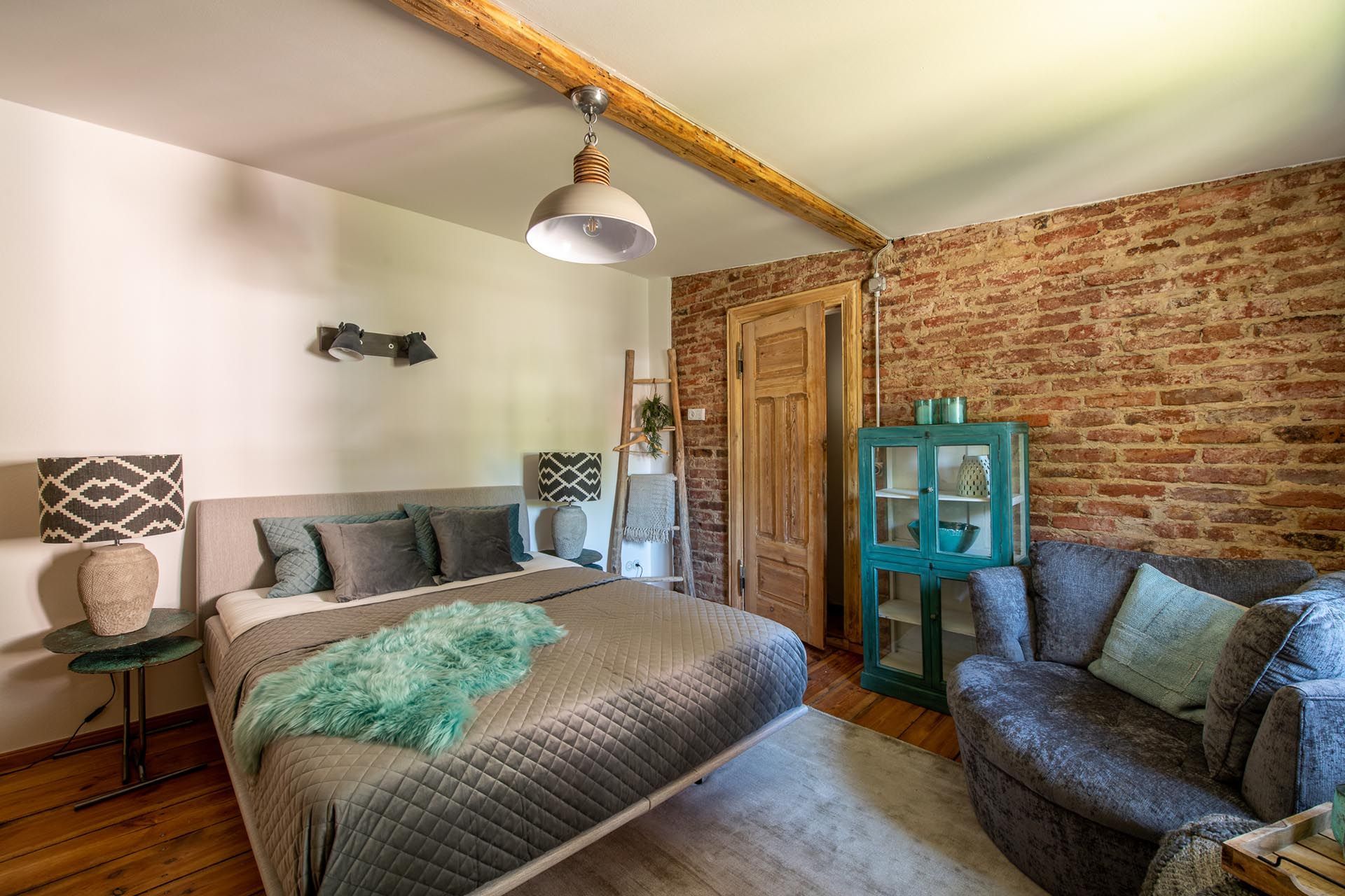 Ein Schlafzimmer mit Bett, Couch, Sessel und Ziegelwand.