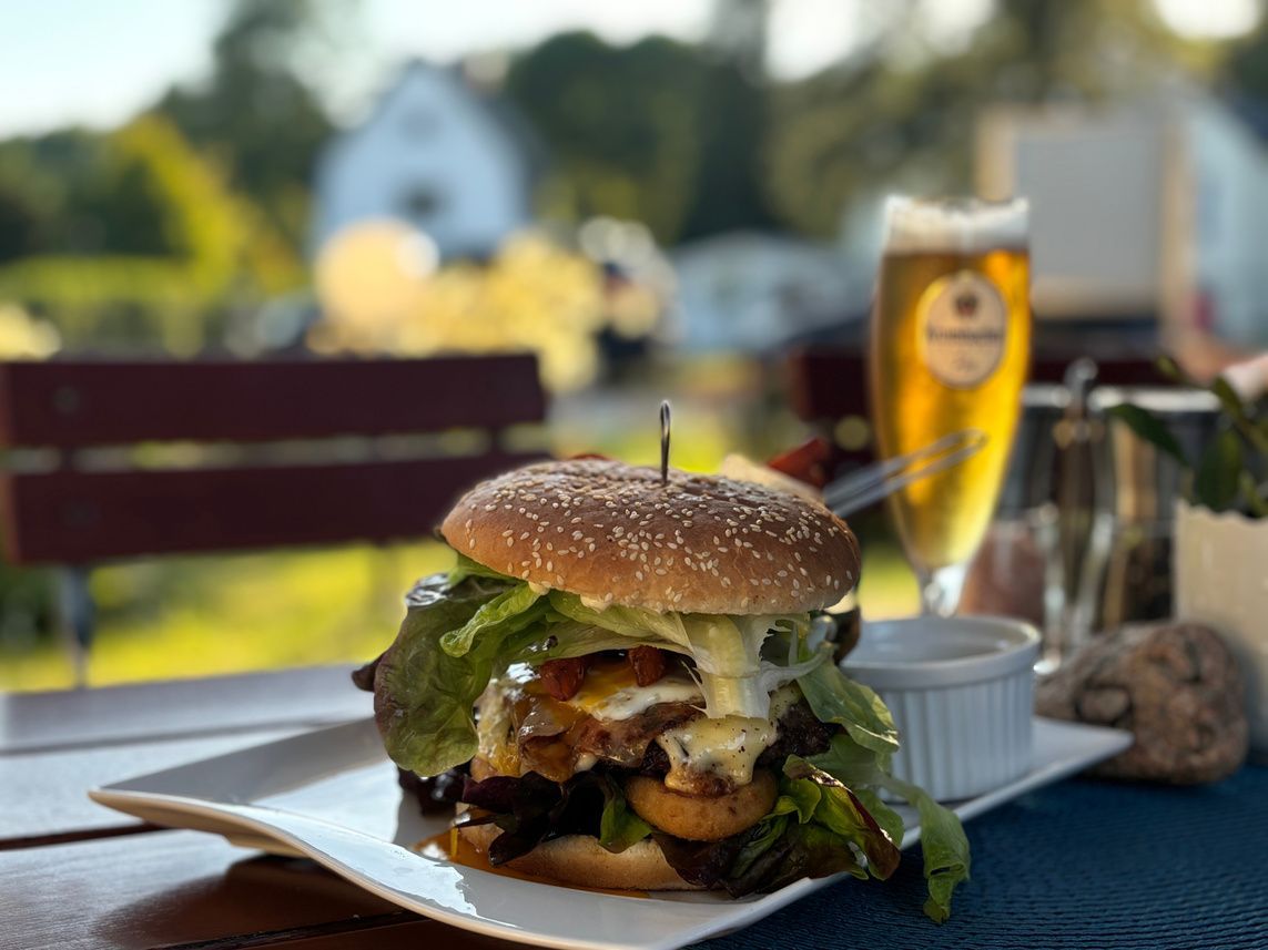 Ein Hamburger liegt auf einem weißen Teller neben einem Glas Bier.