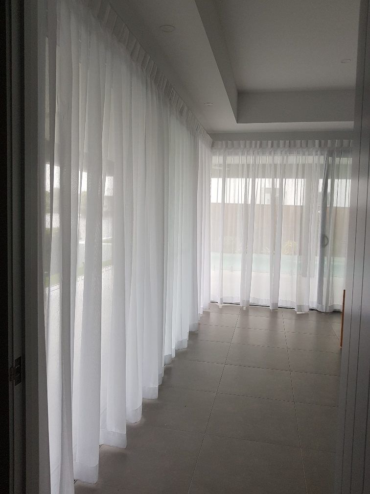 Sheer, floor-to-ceiling white curtains hanging in a modern room with tiled flooring and a view of an outdoor space — Instyle Curtains & Blinds in Bungalow, QLD