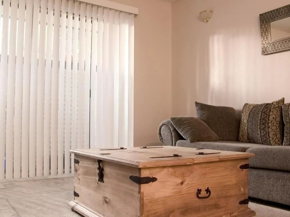 Living Room With Wooden Chest Coffee Table, Gray Couch, and Vertical Blinds — Instyle Curtains & Blinds in Bungalow, QLD