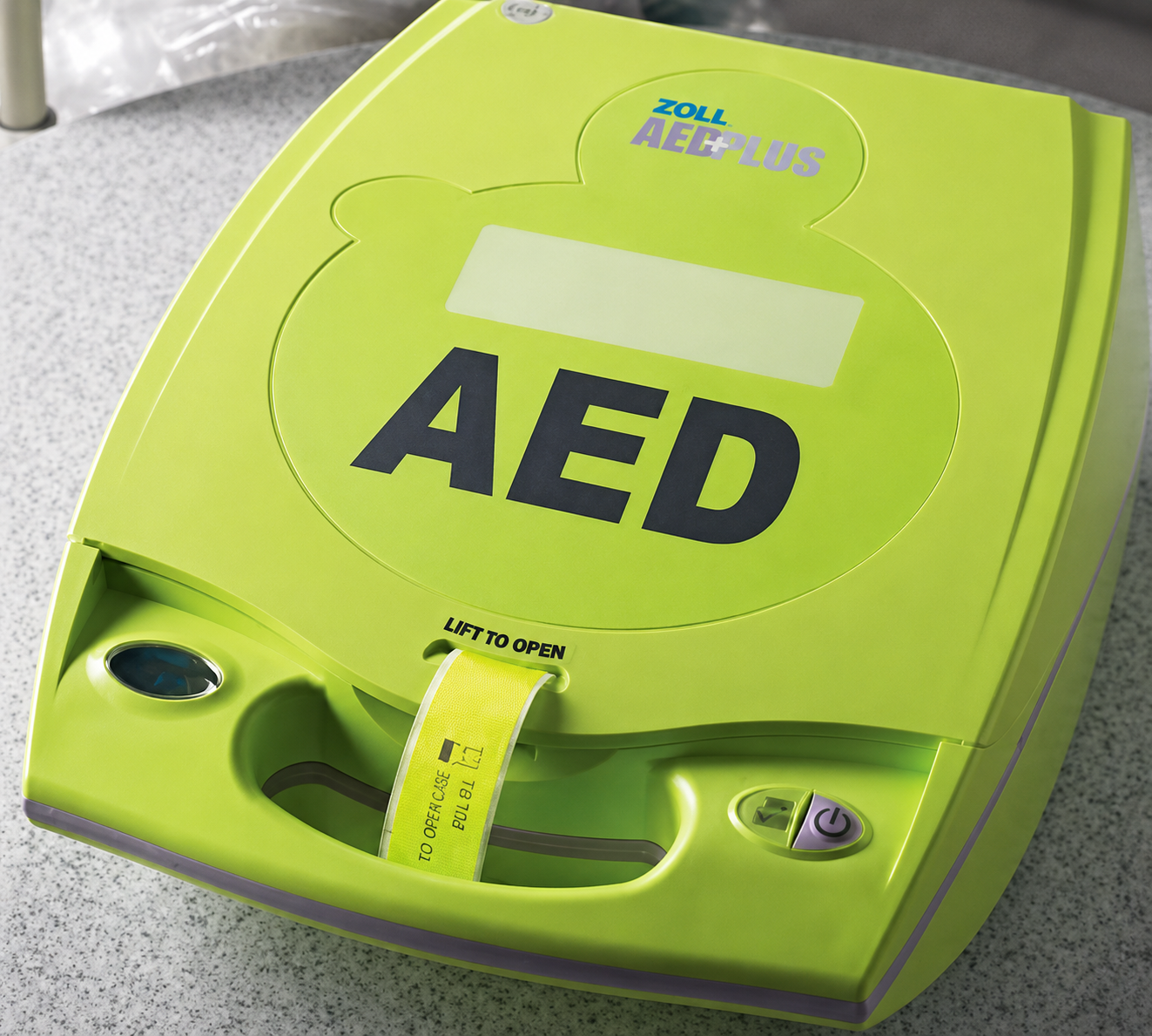 Green AED defibrillator with handle and label on a gray countertop