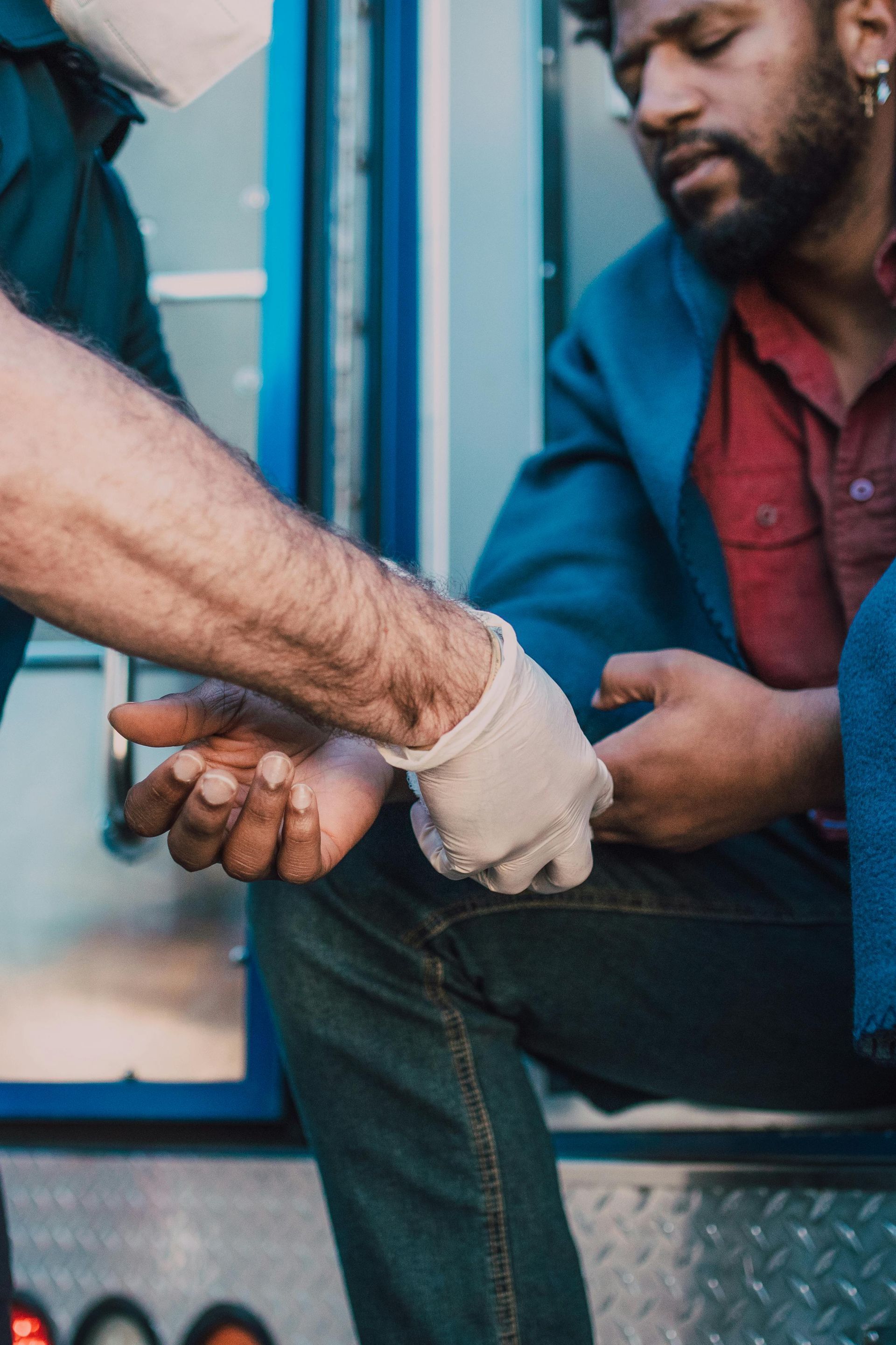 Gloved hands bandaging a seated person’s wrist beside a blue doorway