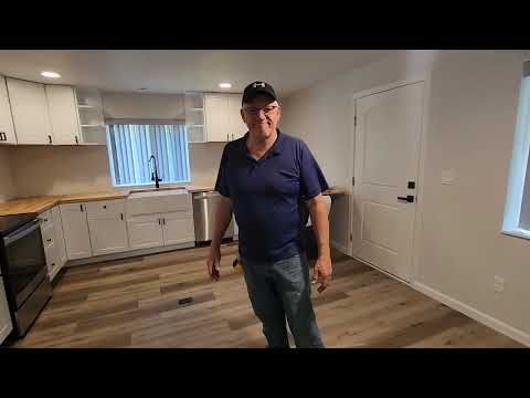 Man standing in a bright empty room with cabinets, wood floors, and a window.